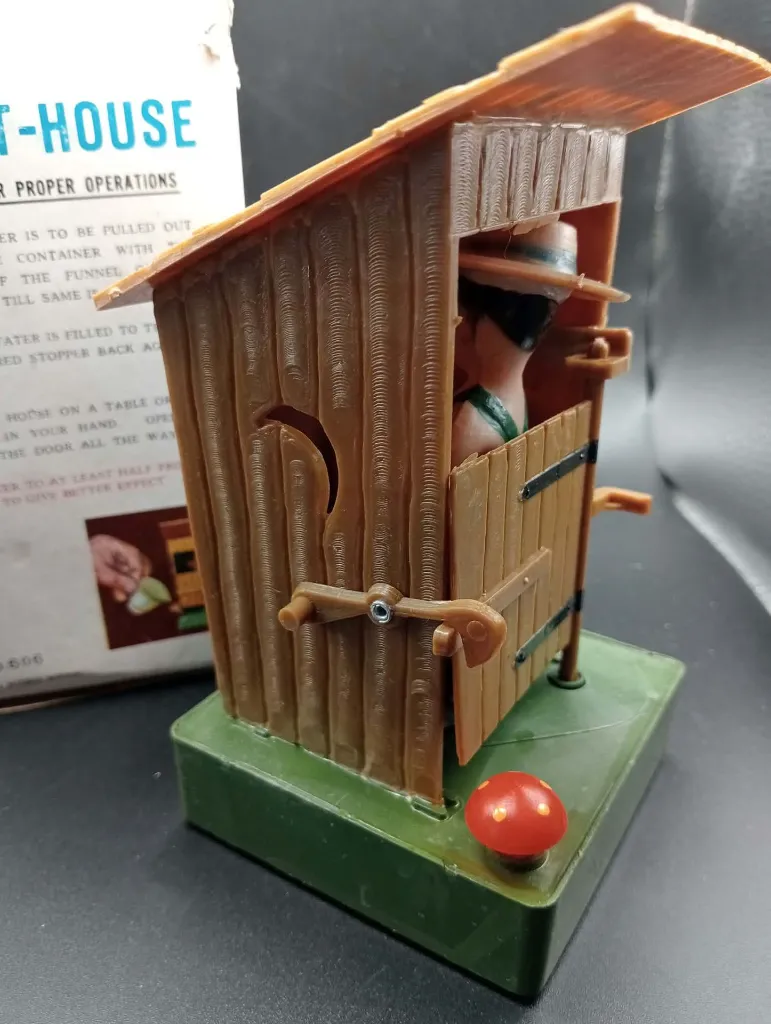 Jouet gag mécanique vintage The Out-House No. 606 en plastique, cabane brune avec personnage intérieur, réservoir d’eau et boîte d’origine
