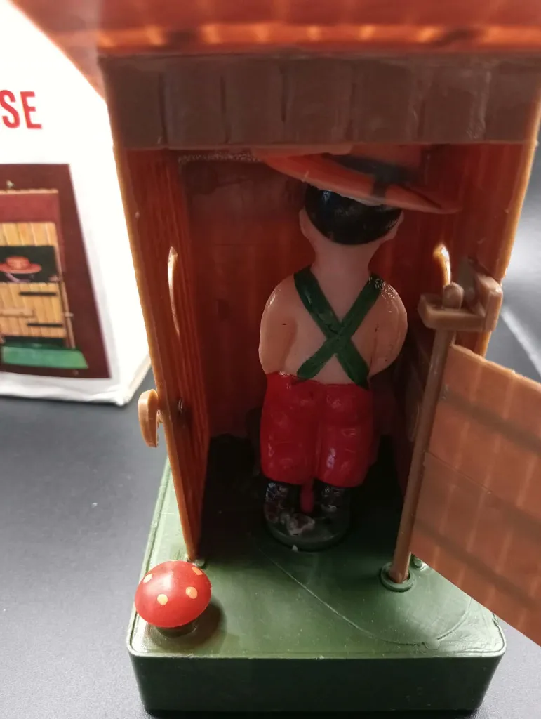 Jouet gag mécanique vintage The Out-House No. 606 en plastique, cabane brune avec personnage intérieur, réservoir d’eau et boîte d’origine