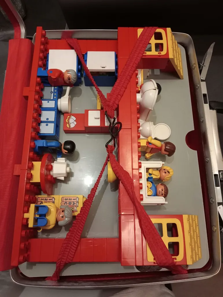 Maison LEGO DUPLO 2770 de 1986 montée dans une valise rouge et argent à façade transparente, avec personnages, cuisine, salle de bains, lits et mobilier