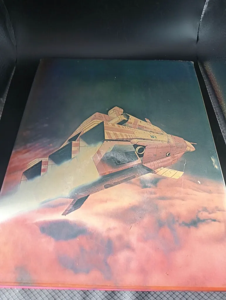 Livro inglês encadernado Starliners de Stewart Cowley com grande nave rosa e amarela sobre fundo alaranjado, ilustrações retrofuturistas e desenhos técnicos