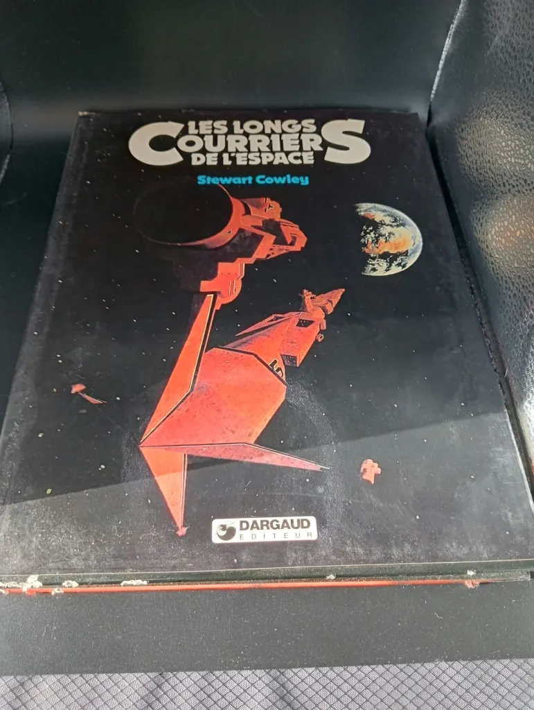 Livre français Les Longs Courriers de l’Espace de Stewart Cowley publié par Dargaud en 1981, couverture noire avec vaisseaux rouges et intérieur illustré en couleurs, reliure fortement rongée