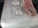 Oude mechanische STB Swiss Made duivenklok van grijs gehamerd metaal met witte wijzerplaat nummer 67992, zijdelingse sluiting met metalen verzegeling en sterk gebarsten rood leren handvat