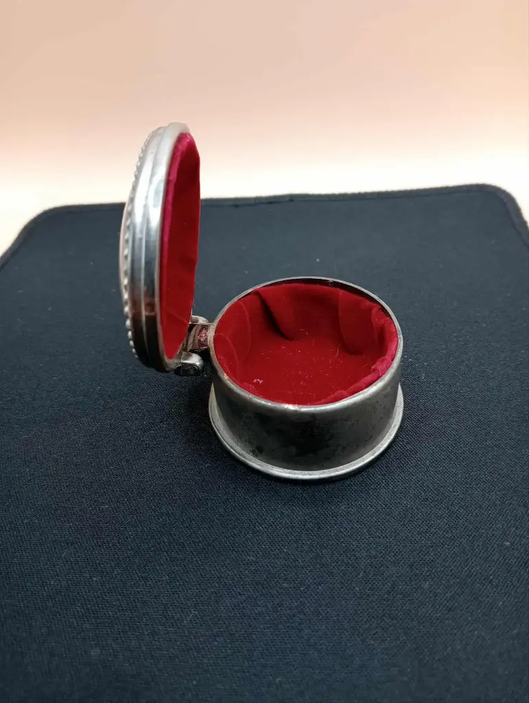 Ovale silberfarbene Metallbox mit rotem Samt innen.